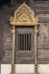 Beautiful window with gilded carved wood panel on heritage landmark Wat Phan Tao buddhist temple facade, Chiang Mai, Thailand