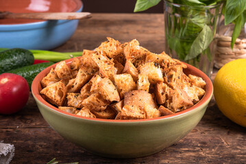 Ciabatta croutons in a bowl close-up on a kitchen table with ingredients for a salad, rustic style.