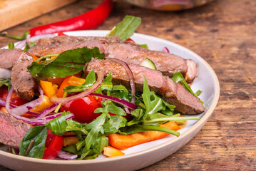 Salad with vegetables, lettuce and pieces of beef steak on a plate, close-up.