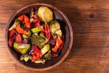 Baked vegetables in a plate, broccoli, zucchini, peppers, onions and tomato - top view, copy space. Vegetarian dish.
