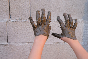 Child's hands in black mud on a gray concrete background. Funny photo. Copy space. 