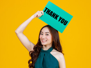 Young happy Asian women smiling and holding green cardboard sign with the word Thank you on top of her head. Standing isolated on bright yellow background