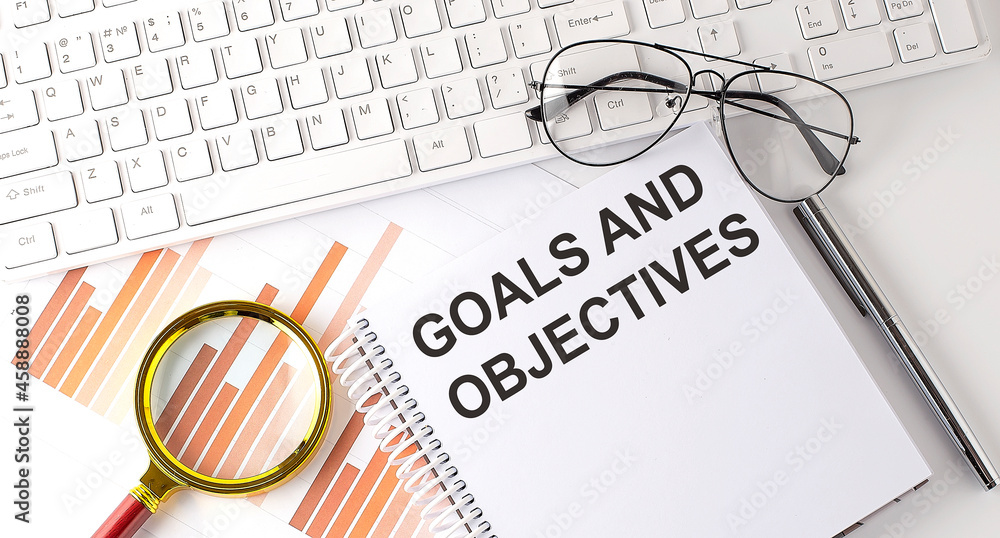 Poster goals and objectives text written on a notebook with keyboard, chart,and glasses