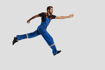 Portrait of young man, male auto mechanic in dungarees running isolated over white studio background. Concept of labor, occupation, funny meme emotions