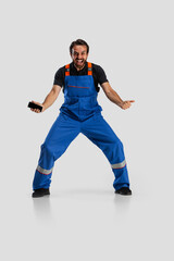 One young excited man, male auto mechanic or fitter in dungarees using phone isolated over white studio background. Concept of occupation, career, funny meme emotions