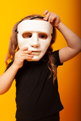 cute little girl child holds a theatrical mask by the face playing a role on the day of the theater, the day of the mime. little actress