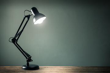 lighting retro desk lamp on old wood table with space of rough cement wall in vintage color tone