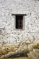 Dark wooden window set in tall whitewashed stone wall with brown dirt stains at the base