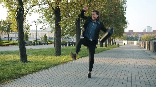 Endless loop of excited young businessman walking and jumping in city street expressing joy on summer day. Positivity and businesspeople concept.