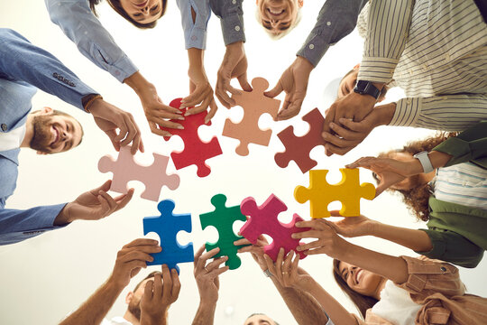 Group of young and mature people making circle of colorful jigsaw puzzle parts, low angle shot from below. Happy business team enjoying teamwork, finding professional solution, starting new enterprise