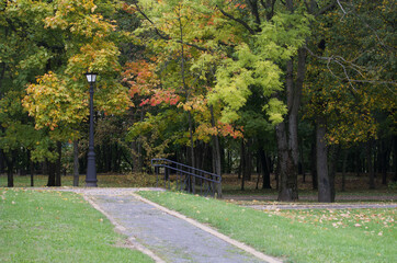 A dirt path in the park and a vintage lantern. The trees show colorful autumn leaves.
