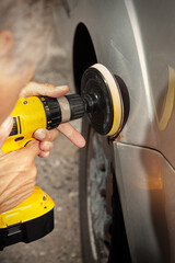 Man in overall working with drill on damage of his car directly on street