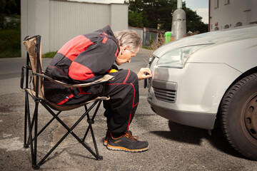 Man in overall working with drill on damage of his car directly on street