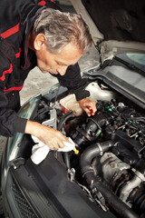 Man in overall working on open engine of his car directly on street