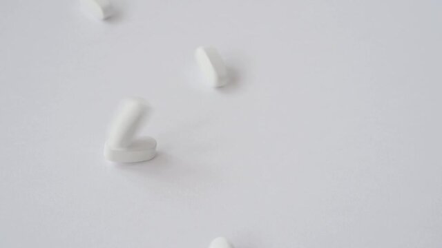 dietary supplement of many white medical vitamin drug tablets pills falling down on bright surface in slow motion