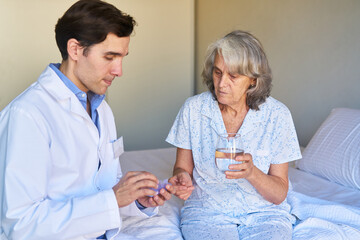 Krankenpfleger verteilt Tabletten an eine kranke Seniorin