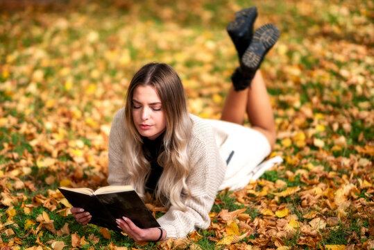 Girl lying on ground in colorful autumn park and reading a book