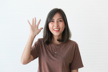 Studio portrait shot of Asian happy young beautiful pretty female teenager model in casual wears smiling look at camera holding right hand up waving greeting say hi or goodbye on white background