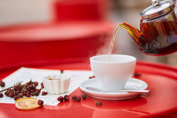 Hot tea in glass teapot and cup, on red background