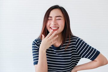 Studio portrait shot of Asian young happy charming cheerful joyful female model wears casual clothing closing eyes smiling laughing holding fingers on chin and hand on waist on white background