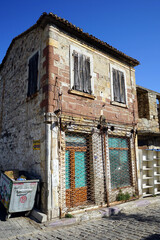 Fototapeta na wymiar Kopfsteinpflaster vor einem alten verfallen Haus mit Mülltonne im Sommer bei blauem Himmel und Sonnenschein in der Altstadt von Foca am Ägäischen Meer in der Provinz Izmir in der Türkei