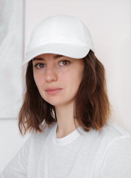 Female Model Wearing A White Baseball Cap. White Cap Mockup, Template For Picture, Text Or Logo. Girl Holding Visor Of Cap. Free Space, Copy Space.