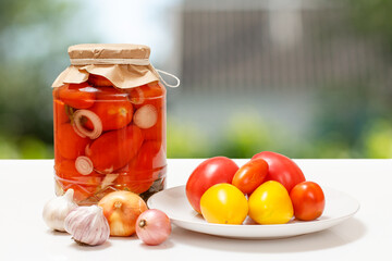 Pickled tomatoes in glass jars on blurred background.