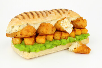 Fish and chips sandwich with battered cod fish and mushy peas in a panini bread roll