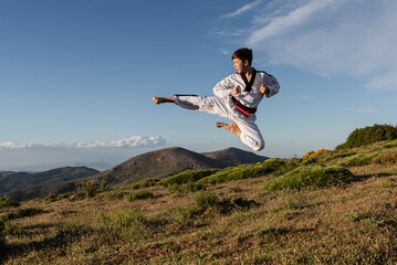 Karate boy in white kimono kicks in the air while practicing martial arts outdoors. Sports concept.