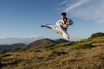 Foto auf Acrylglas Karate boy in white kimono kicks in the air while practicing martial arts outdoors. Sports concept. © MANUEL