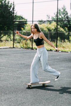 Cute teen girl rides a skateboard on a sports field