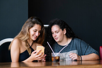 Two girls sharing a drink and laughing looking at the phone