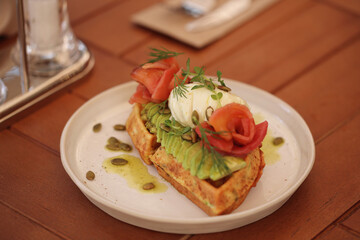 waffles with avocado, poached egg and fish are on the table