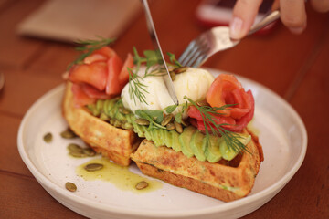 waffles with avocado, poached egg and fish are on the table