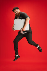 Full length portrait of stylish red-bearded man, barber or hair cutter jumping isolated on red studio background.