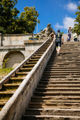 Kuks, East Bohemia, Czech Republic, 10 July 2021: well or a fountain with statues of Triton Greek god of sea, staircase with water cascade at sunny summer day, baroque castle and hospital Kuks.