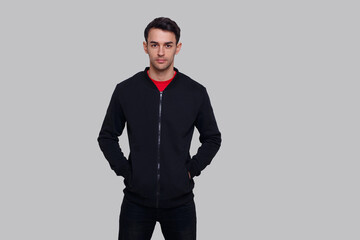 Fototapeta premium Frontal image of a smiling young brunette man in dark blue jumper and jeans, isolated over grey background.