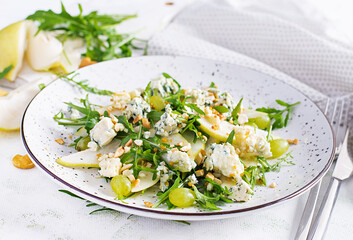 Salad of pear, blue cheese, grape, arugula and nuts with spicy dressing on a light background. Healthy eating.