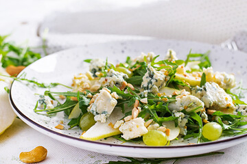 Salad of pear, blue cheese, grape, arugula and nuts with spicy dressing on a light background. Healthy eating.