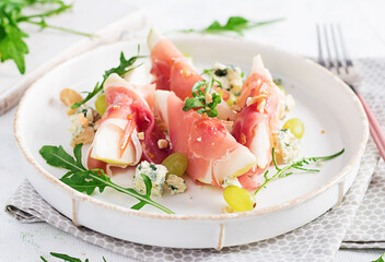 Appetizer with pear, blue cheese and prosciutto ham for holidays on a white plate.