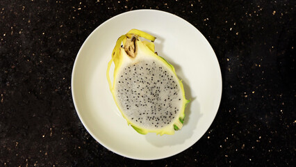 Flay of a white plate placed in the middle, with half a cut yellow dragon fruit on it.