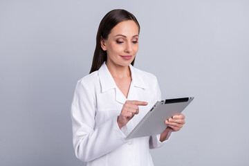 Portrait of attractive focused cheery nurse doctor using tablet searching medical information isolated over grey pastel color background