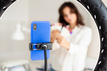 Young woman manicurist master blogger recording video using ring lamp and smartphone, talking and gesturing at camera, explain something. Online Master class, training courses, lesson via internet