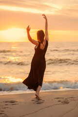 Fototapeta na wymiar Beautiful woman dancing in dress near the sea at sunset