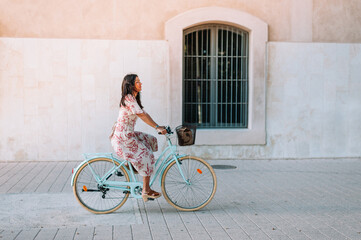 Fototapeta premium Full body portrait of a beautiful stylish woman riding with retro bicycle outdoors on the industrial urban background