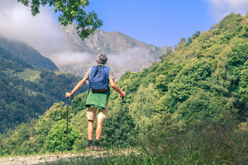 Middle age man walking in the mountain forest. Male with backpack do hike in the nature. Guy goes trekking outdoor in a beautiful park. Outdoors sport. Freedom, relax, leisure and lifestyle concept.