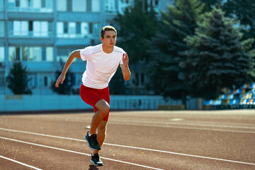 Obraz premium Young Caucasian man, male athlete, runner practicing alone at public stadium, sport court or running track outdoors. Summer sport games.
