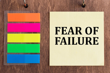 text fear of failure on yellow card next to colored stickers on wooden table. business concept