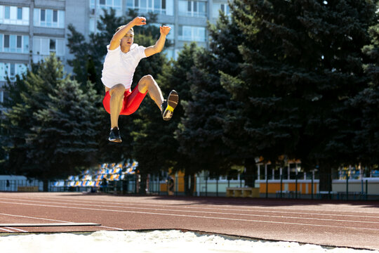 Young Caucasian sportive man, male athlete, runner jumping high at public stadium, sport court or running track outdoors. Summer sport games.