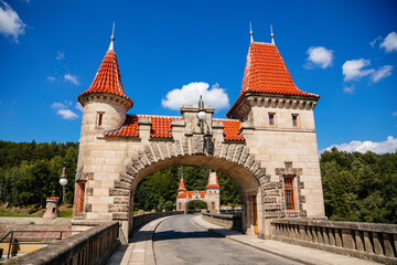 Fototapeta premium Bila Tremesna, Czech Republic, 10 July 2021: Amazing colorful view of Les Kralovstvi historic hydraulic water dam with orange water in river Elbe, Kingdom Forest, road with towers at sunny summer day